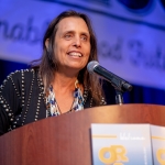 Winona LaDuke speaking at a lectern in front of a blue background
