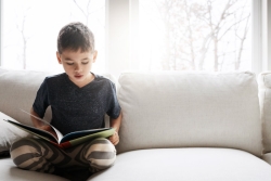 Child sitting cross legged on a white couch reading a picture book
