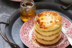 Stack of cheese pancakes on a red and white patterned plate with honey on top 