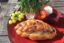 Pumpkin cranberry challah on a red plate with a plant and apples and grapes 