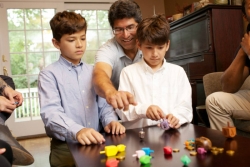 Father and two sons playing dreidel on a wooden table 