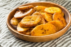 Wooden bowl of fried sweet plantains on a striped grey and white tablecloth 