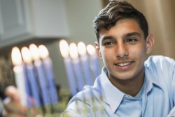 Teenage boy lighting blue Hanukkah candles