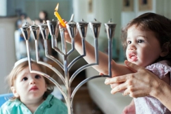 Two young children lighting a silver menorah
