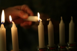 Hand lighting white Hanukkah candles in a menorah