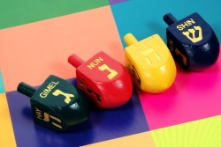 Four colorful wooden dreidels on a brightly colorblocked surface 