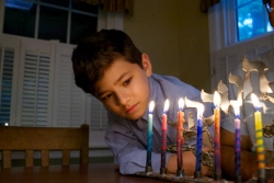 Young boy looking at a lit menorah with colorful candles