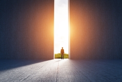 person standing in a doorway looking out at a bright light representing hope