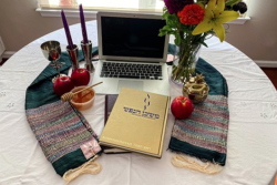 a laptop on a table with apples and honey, kiddish cup, candle sticks and flowers