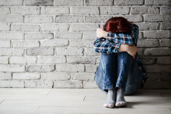 an image of a woman sitting with her head on her knees, up against a brick wall