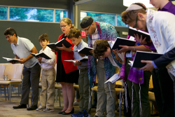 Photo of a group of people of different genders and ages holding prayer books at bent over praying