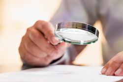 Photo of a person holding a magnifying glass over a piece of paper