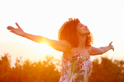 Photo of a woman standing with arms wide open and the sun shining behind