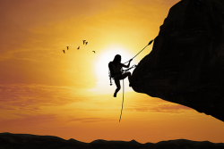 Photo of the silhouette of a person climbing on the side of a mountain