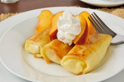 Plate piled with cheese blintzes topped with peaches and whipped cream