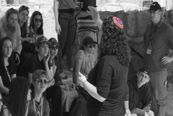 Black and white image of Cantor Katie Oringel teaching students outdoors in Israel with only her rainbow kippah appearing in color