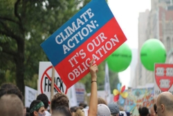 Hand holding up a sign that reads Climate Action Is Our Obligation at a protest rally 