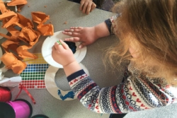 Childs hands working on some sort of craft surrounded by paint and paper