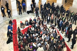 120 clergy and activists sitting on the floor of a Senate office building while Capitol police look on 
