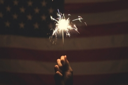 hand holding a lit sparkler in front of an American flag