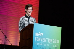 Glory Mayreis stands at a podium bearing the name NFTY Convention