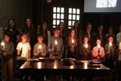 Graduating seniors standing behind fifth graders as they pass candles down to the younger class