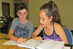A boy and girl sitting at a table together and working through a notebook