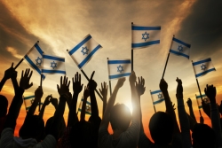 Hands in shadow of sunset holding Israeli flags on sticks