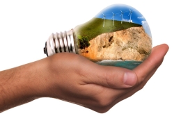 Graphic of a hand holding a lightbulb that appears to contain a mountain and windmills