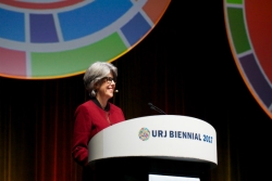 URJ VP of Youth Miriam Chilton in a red blazer in front of the URJ Biennial logo