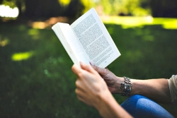 Closeup of a womans hands holding a book as she reads on a lawn