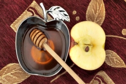 Apple shaped bowl of honey with a honey dipper in it and half an apple on a table next to it 