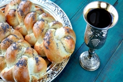 Two loaves of challah on a silver platter next to a cup of wine 