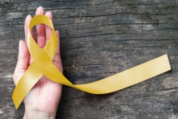 Hand holding a yellow suicide awareness and prevention ribbon against a wooden table background