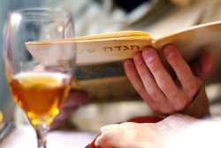 A wine glass during a Seder. A woman reads from a Haggadah