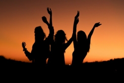 Silhouette of three women cheering against a sunset