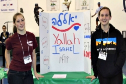 Two smiling teen girls next to a posterboard advertising the Yallah Israel club 