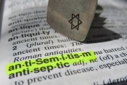 Dictionary open to anti-Semitism, with that word highlighted in neon yellow and a Jewish star stamp resting on the page