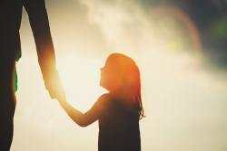 Sunset profile of a child holding the hand of an adult and looking up toward them