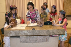 Young children gathered around watching a woman read from a Torah scroll