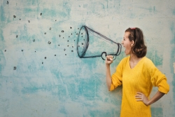 Young woman shouting into a megaphone that is drawn on the wall next to her