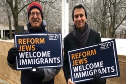 Danny Cooper and another man holding signs that say REFORM JEWS WELCOME IMMIGRANTS