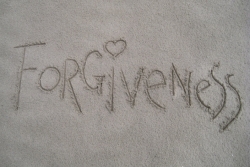 The word forgiveness written in the sand with a heart as the dot over the letter i