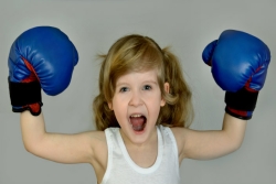 Elementary school-aged girl wearing blue boxing gloves with hands above her head