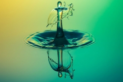 Closeup of a droplet hitting a surface of water and splashing up while reflecting down