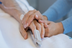 Hospital visitor clasping the hand of hospital patient in bed