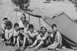 Black and white image of a group of smiling children beneath a small tent in a desert setting