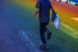 Child running through a rainbow reflection holding a transgender rights flag
