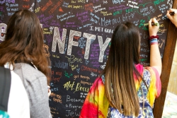 Teens with their backs to the camera as they write with chalk on a board that says NFTY