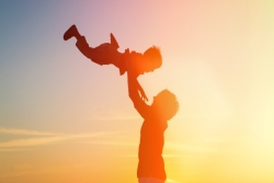 Adult holding small child joyfully overhead with sunset in the background